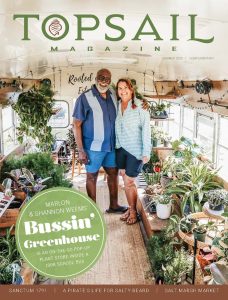 A smiling man and woman stand inside a school bus filled with lush green plants, pots, and gardening supplies. The bus is bright with sunlight streaming through the windows. The magazine is titled "Topsail Magazine.